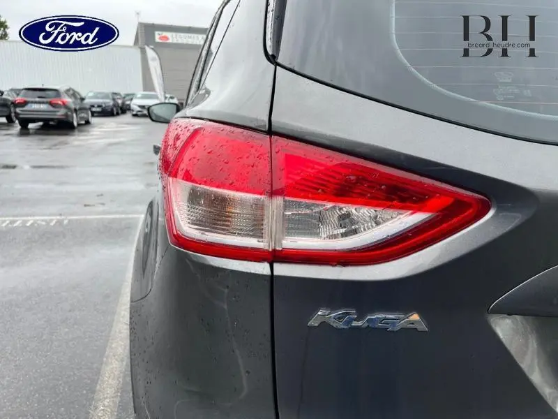 Gros plan sur le feu arrière gauche d'un Ford Kuga gris Magnetic avec logo Kuga visible sous la pluie.