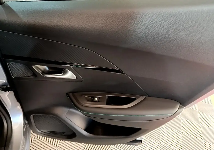 Gros plan sur la porte côté gauche gris clair de la Peugeot 2008 avec surpiqûres bleues et poignée argentée.