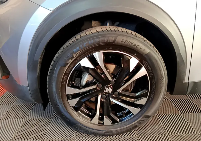 Gros plan sur la roue avant gauche du Peugeot 2008 gris clair avec jante alliage noire et argentée.