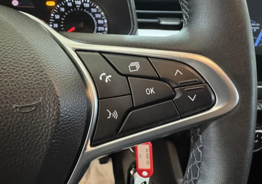 Gros plan sur le volant noir de la Renault Clio Business avec commandes multifonctions et tableau de bord partiellement visible.