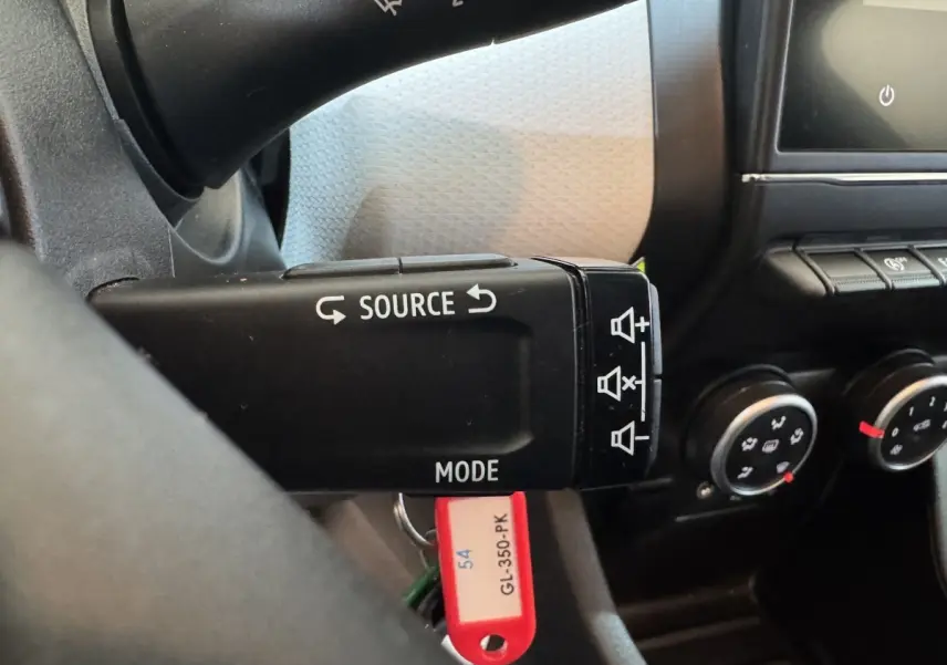 Gros plan sur la commande au volant noir de la Renault Clio Business blanc, avec boutons source et mode visibles.