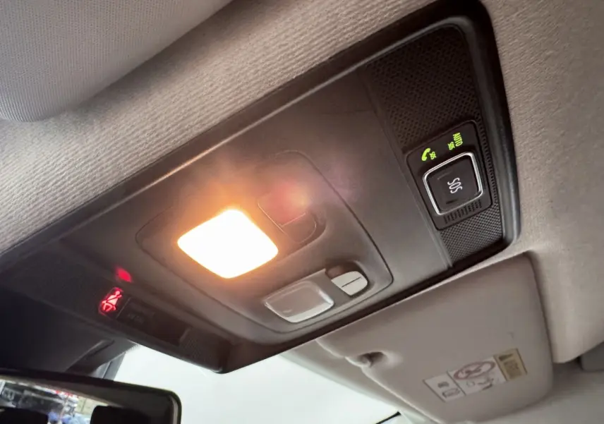 Plafonnier intérieur allumé avec bouton SOS et éclairage d'ambiance dans une Renault Clio blanc, vue en léger contre-plongée.
