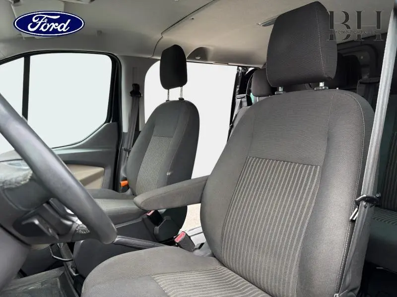 Vue intérieure avant du Ford Transit Custom Fourgon noir, montrant les sièges conducteur et passager en tissu gris.