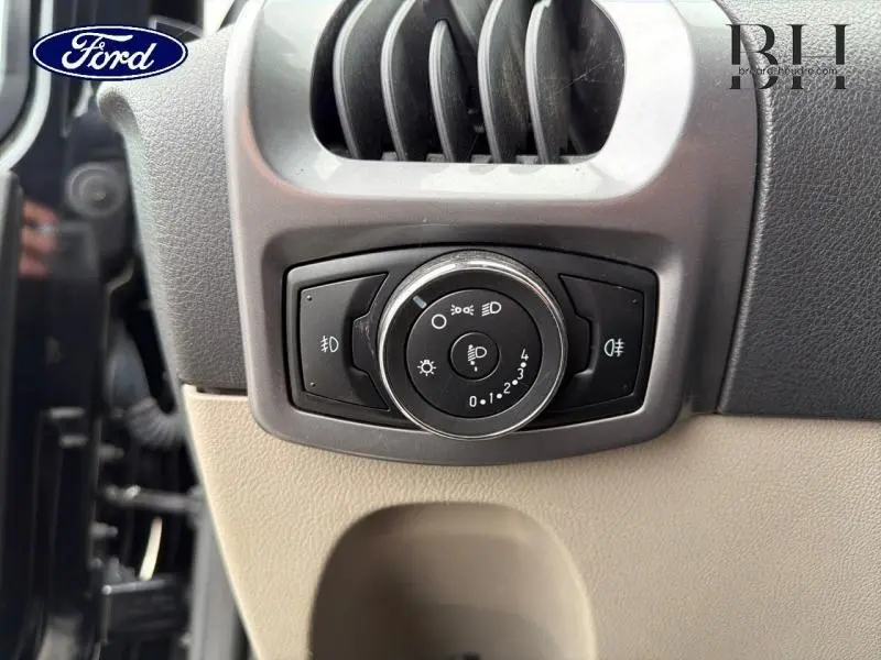 Gros plan sur le bouton de commande des phares noir et argenté dans l'habitacle beige du Ford Transit Custom noir.