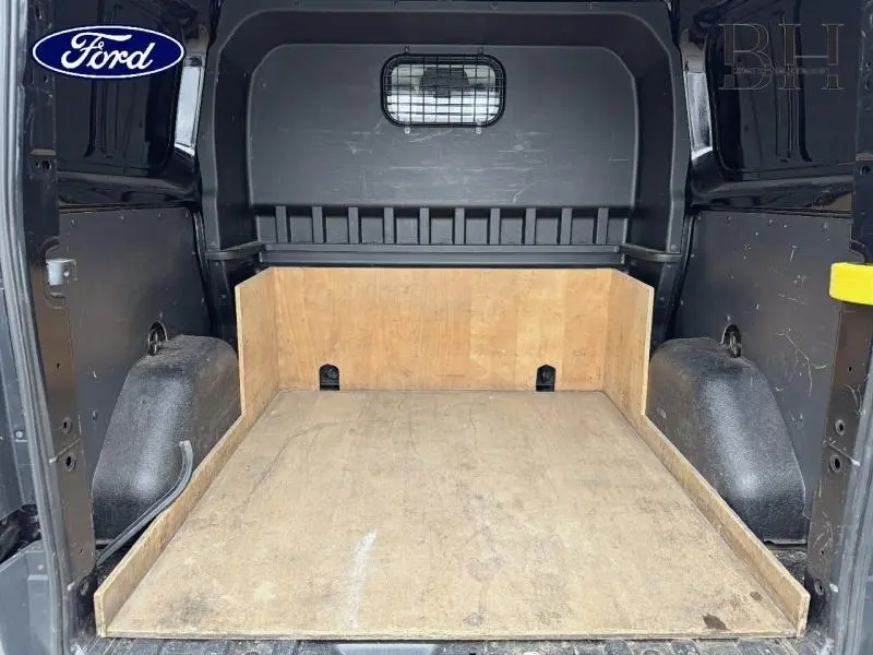 Vue intérieure arrière du fourgon Ford Transit Custom noir, montrant l'espace de chargement avec plancher et parois en bois.