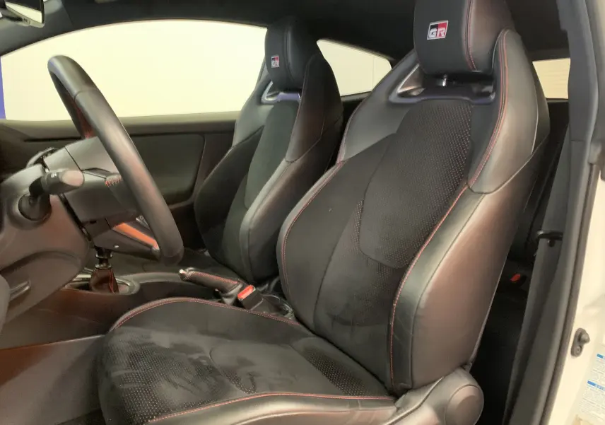 Vue intérieure côté conducteur de la Toyota Yaris GR 1.6 VVT-I avec sièges sport noirs et surpiqûres rouges.