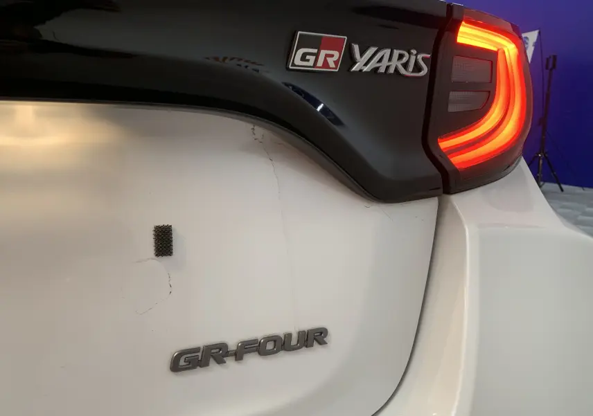 Gros plan arrière droit d'une Toyota Yaris GR blanche métal avec feux allumés et badges GR Yaris et GR-FOUR visibles.