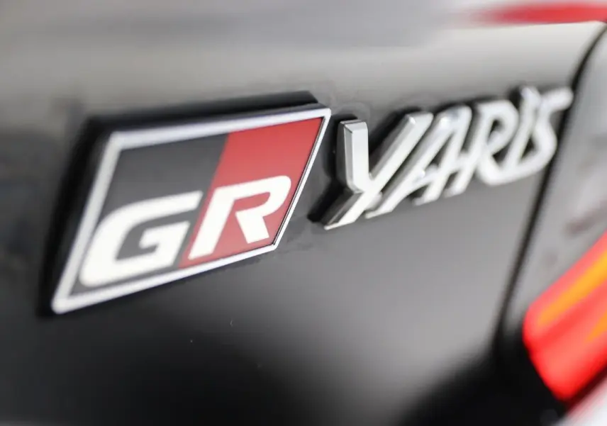 Gros plan sur l'emblème GR et le logo Yaris sur une carrosserie noire avec un détail rouge vif.