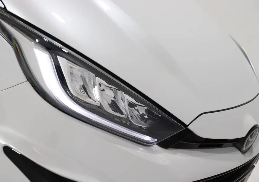 Gros plan sur le phare avant gauche et la calandre noire d'une Toyota Yaris blanc métal.