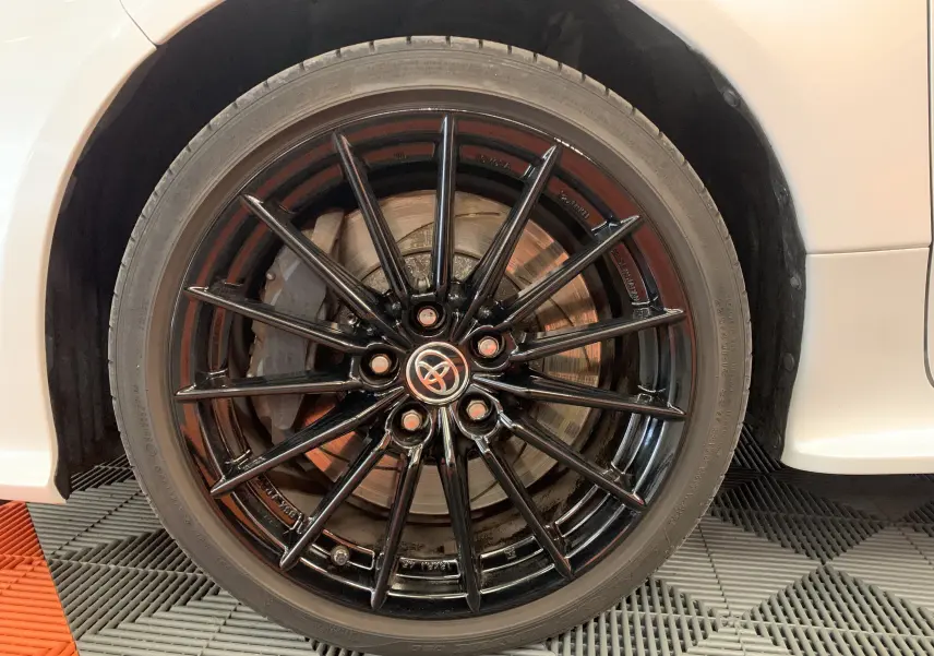 Gros plan sur la roue avant droite d'une Toyota Yaris blanche métal avec jante alliage noire multi-branches.