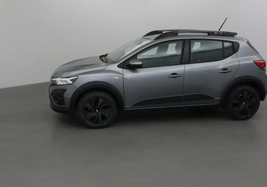 Profil côté gauche d'une Dacia Sandero Stepway gris schiste 2025 avec barres de toit et protections noires sur les passages de roues.