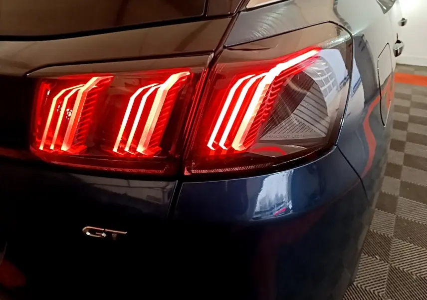 Gros plan sur le feu arrière droit allumé d’un Peugeot 3008 GT bleu, avec logo GT visible sur la carrosserie.