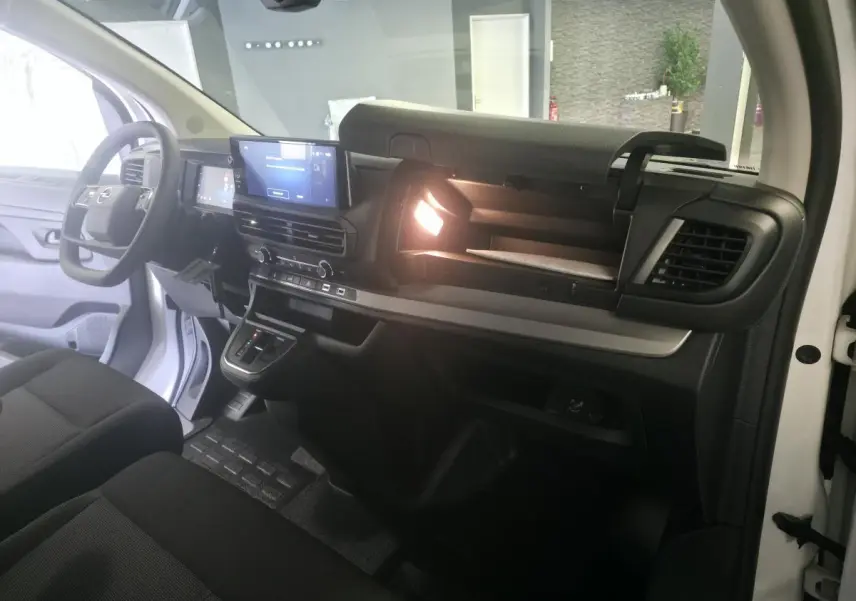 Vue intérieure côté passager de l'Opel Vivaro blanc 2025, tableau de bord avec écran tactile et boîte à gants ouverte éclairée.