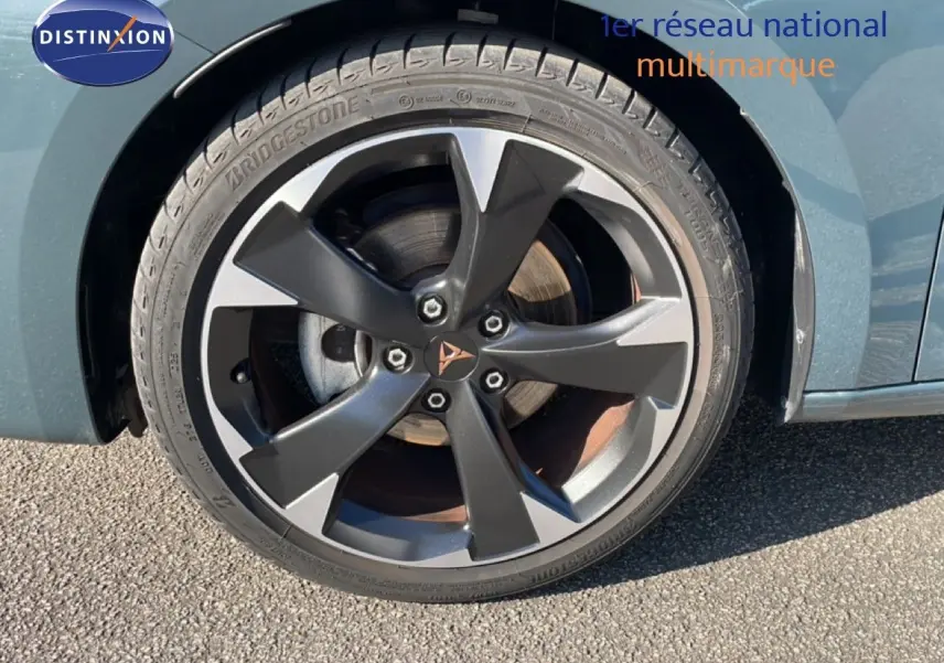 Gros plan sur la roue avant gauche d'une CUPRA Leon 1.5 eTSI 150CH DSG bleu Fjord avec jante alliage noire et grise.