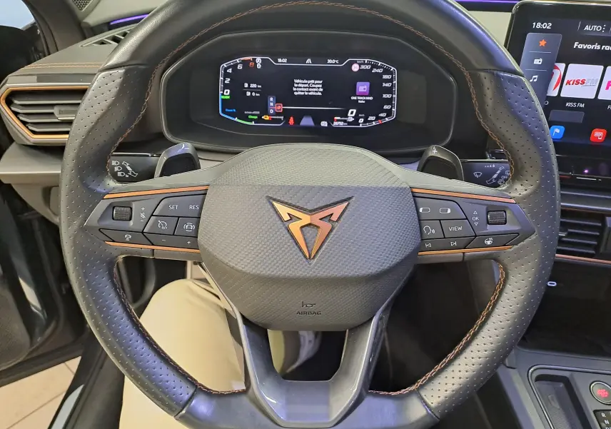 Vue rapprochée du volant en cuir perforé avec logo CUPRA cuivré et tableau de bord numérique du Formentor gris magnétique 2024.