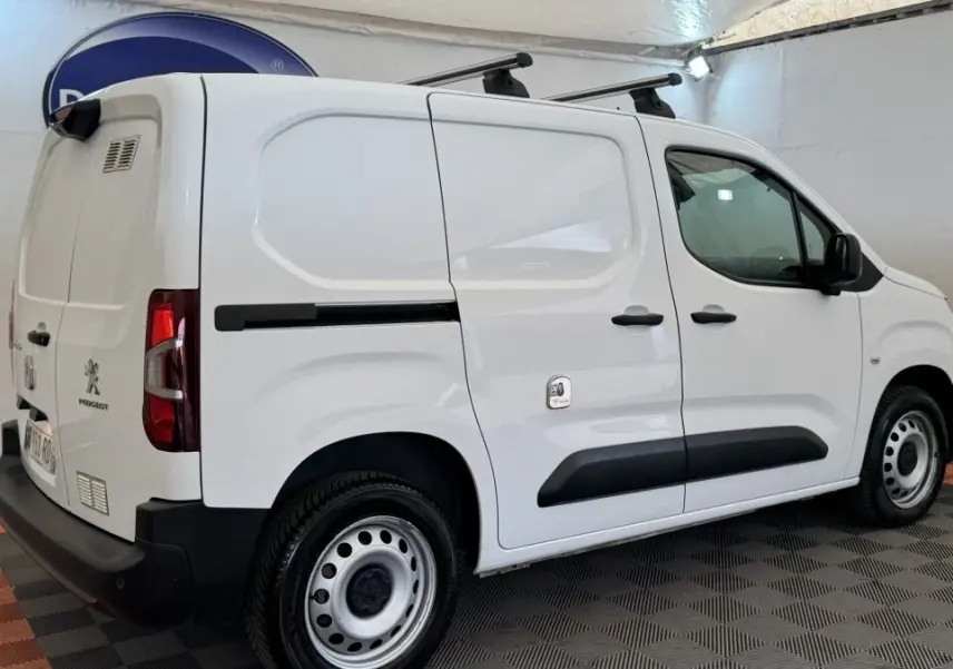 Vue 3/4 arrière droite d'un utilitaire Peugeot Partner blanc avec barres de toit et jantes acier.