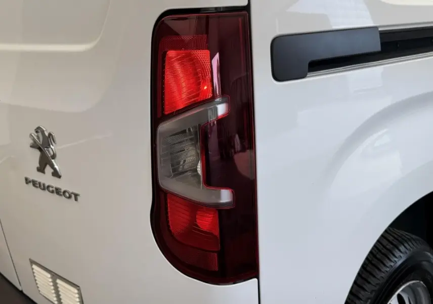 Vue arrière droite du Peugeot Partner blanc, mettant en valeur le feu arrière et le logo Peugeot sur la porte.