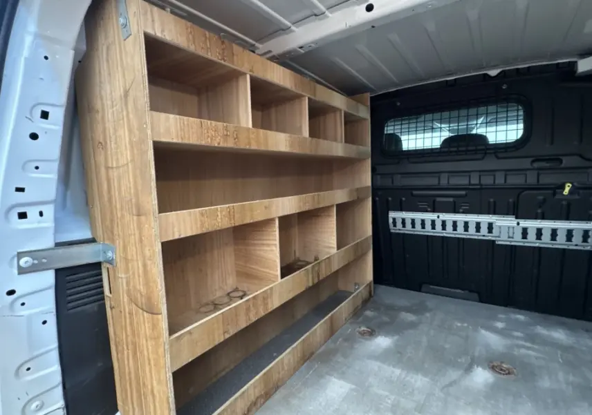 Intérieur arrière du Peugeot Partner blanc 2021, vue côté gauche montrant étagères en bois et cloison noire pleine.