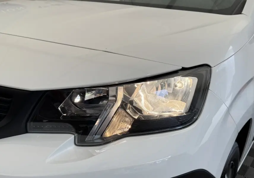 Gros plan sur le phare avant droit du Peugeot Partner blanc, mettant en valeur le design moderne et la calandre noire.
