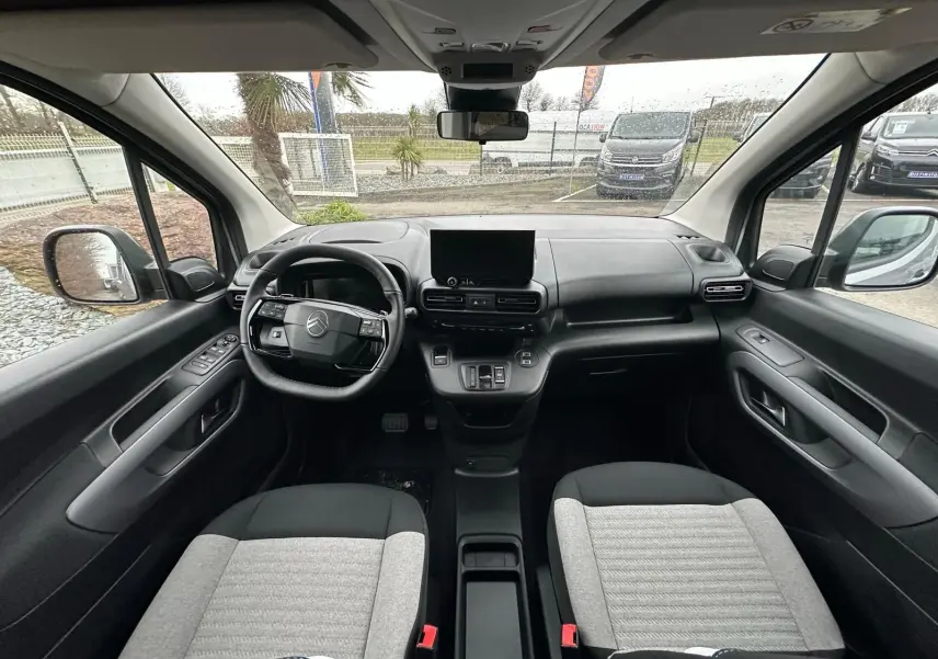 Vue intérieure avant du Citroën Berlingo 2025, sièges bicolores gris et noir, tableau de bord moderne avec écran central.