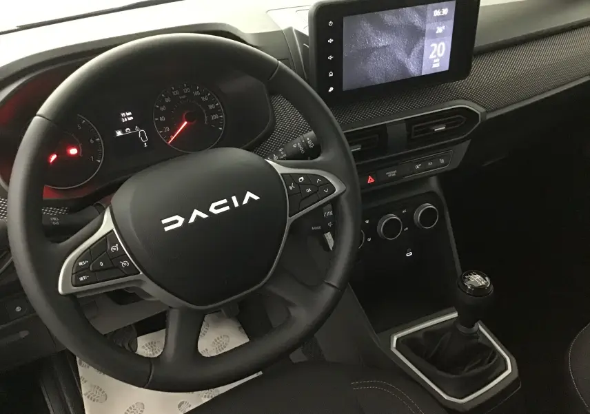 Vue intérieure centrée sur le volant DACIA et la console avec écran tactile et levier de vitesses manuelle.