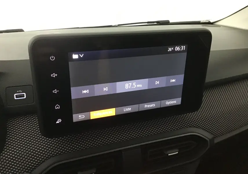 Écran tactile central de la Dacia Sandero Stepway 2025 affichant la radio FM à 87,5 MHz sur un tableau de bord texturé.