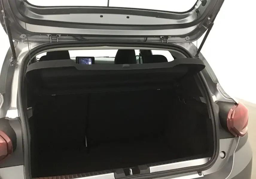 Coffre ouvert vu de l'arrière droit d'une Dacia Sandero Stepway gris schiste, intérieur sombre et tablette visible.