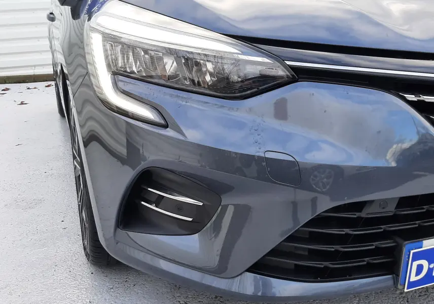 Gros plan sur le phare avant gauche et la calandre d'une Renault Clio V gris titanium, version TCE 90 Intens X-Tronic.