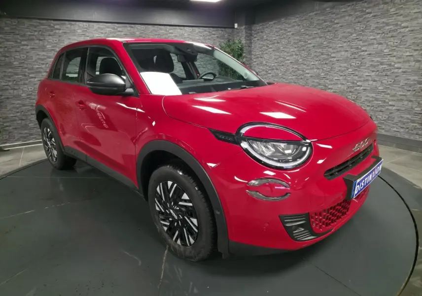 Vue 3/4 avant droite d'une FIAT 600 rouge avec phares LED et jantes bicolores en intérieur showroom.