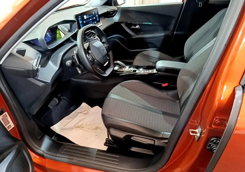 Intérieur de la Peugeot 2008 orange vue côté conducteur, montrant sièges tissu, volant cuir et tableau de bord digital.