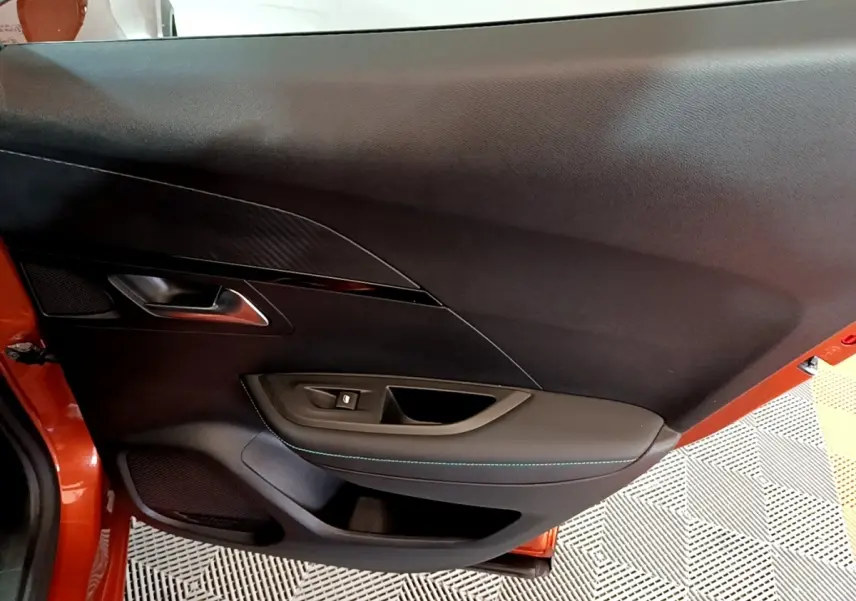 Vue intérieure de la porte côté gauche d'un Peugeot 2008 orange, avec garniture noire et surpiqûres bleues.