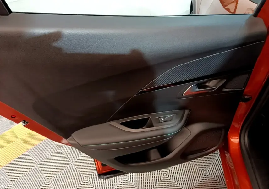 Vue rapprochée de la porte avant gauche orange du Peugeot 2008 2021, mettant en valeur les finitions intérieures noires et le bouton de lève-vitre.