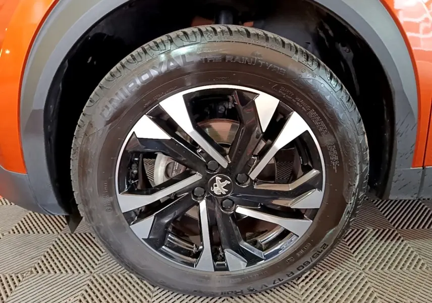 Gros plan sur la roue avant droite orange d’un Peugeot 2008 avec jante alliage noire et argentée au design moderne.