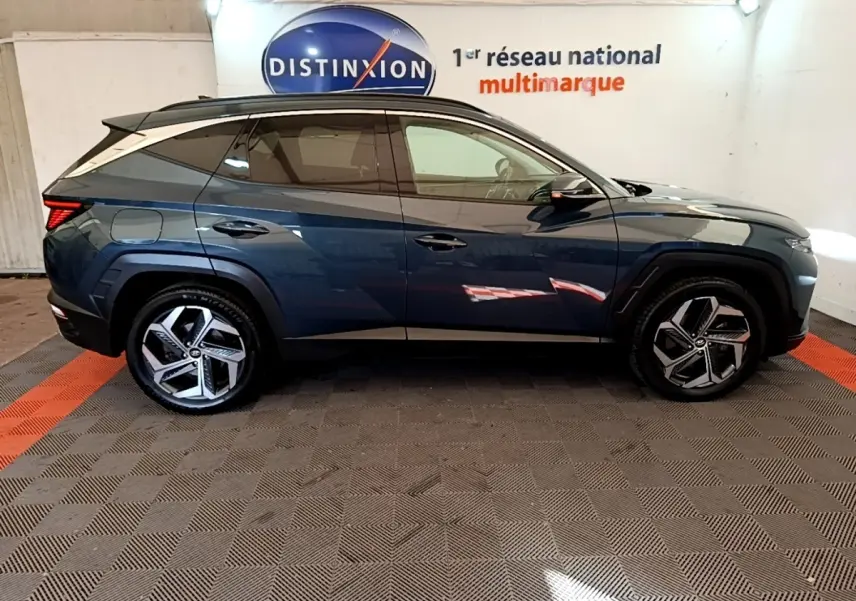Profil côté droit du Hyundai Tucson bleu 2023 avec jantes alliage et vitres teintées dans un showroom.