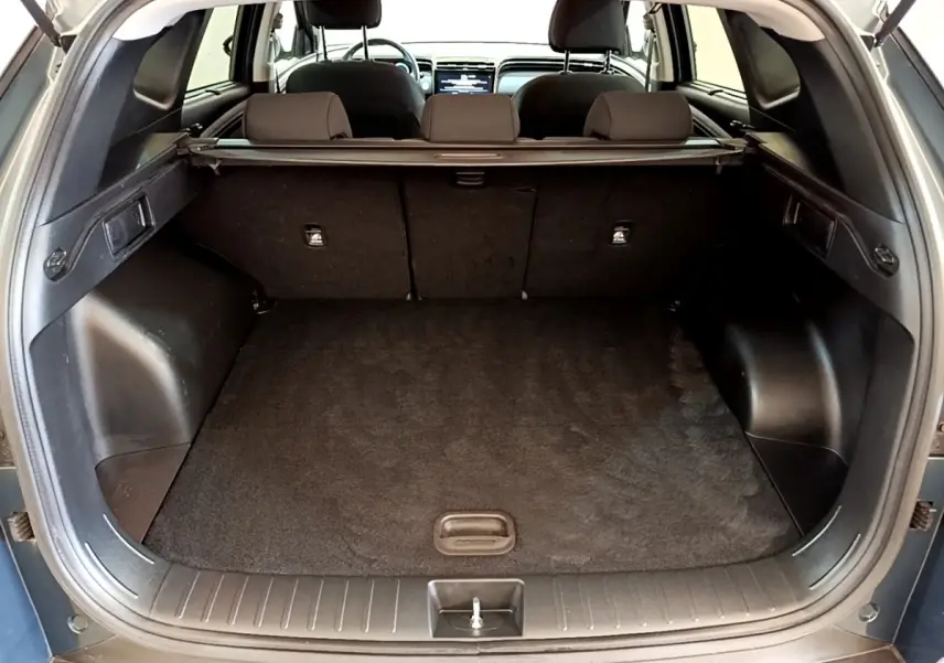 Vue arrière du coffre ouvert du Hyundai Tucson bleu 2023, montrant l'espace de chargement et la tablette cache-bagages.
