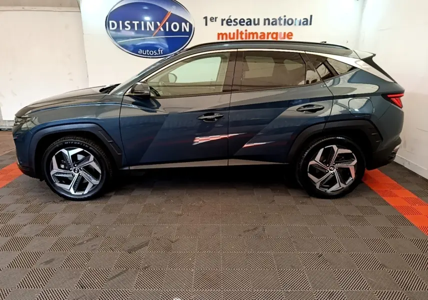 Vue de profil côté gauche du Hyundai Tucson bleu 2023 avec jantes alliage et toit noir contrasté.