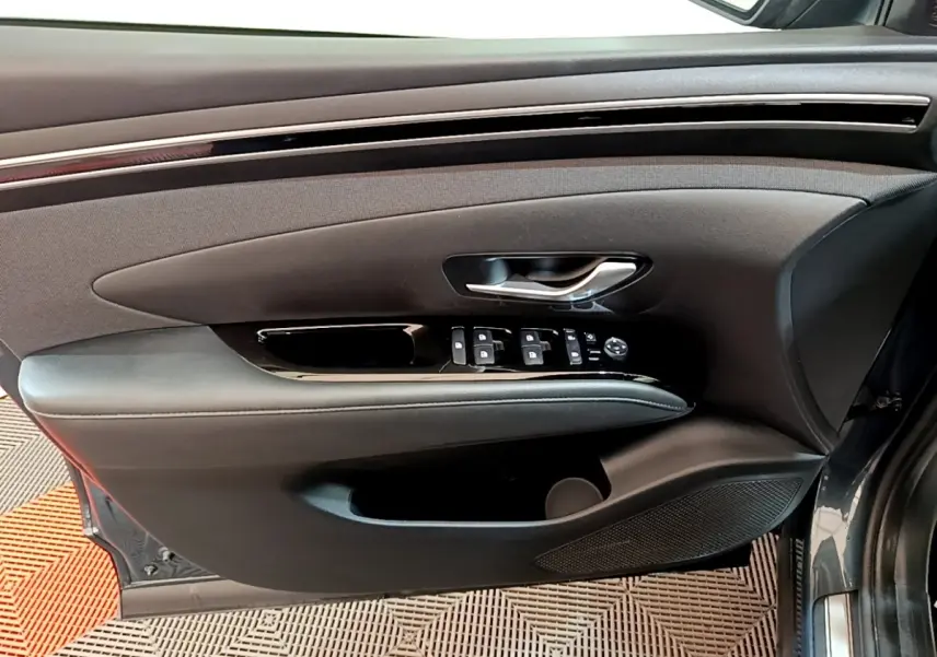 Vue intérieure côté gauche de la porte avant d'un Hyundai Tucson bleu 2023 avec commandes de vitres et poignée argentée.