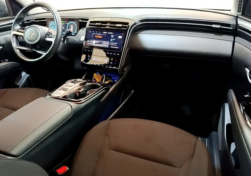 Vue intérieure côté conducteur du Hyundai Tucson 2023, tableau de bord noir avec écran tactile central et volant cuir.