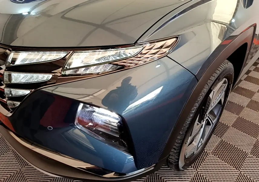 Vue rapprochée avant droite du Hyundai Tucson bleu 2023, mettant en valeur ses phares LED et la calandre distinctive.