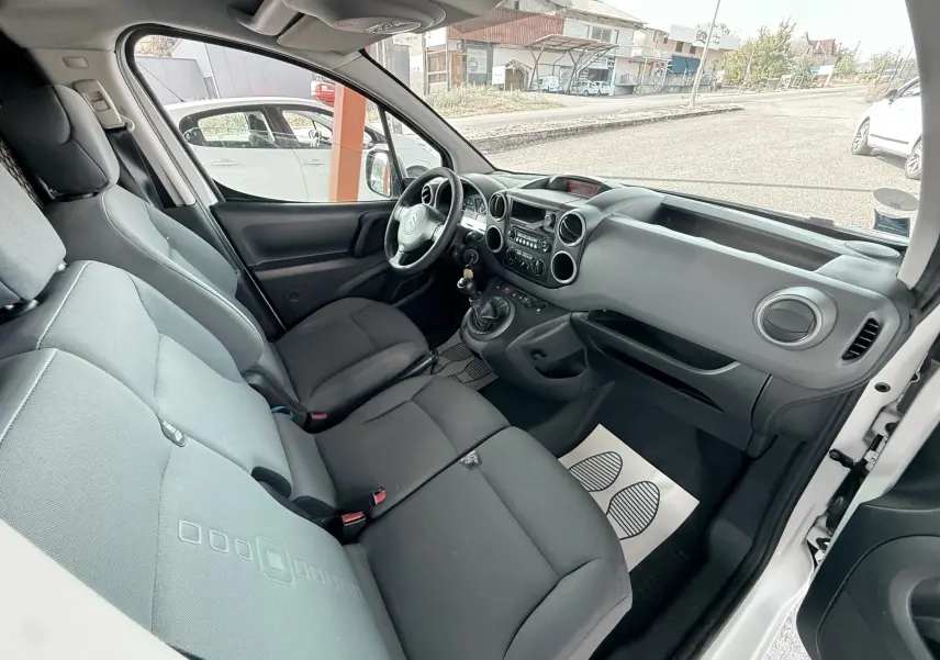 Vue intérieure côté conducteur du Citroën Berlingo blanc, montrant le tableau de bord et les sièges en tissu gris.