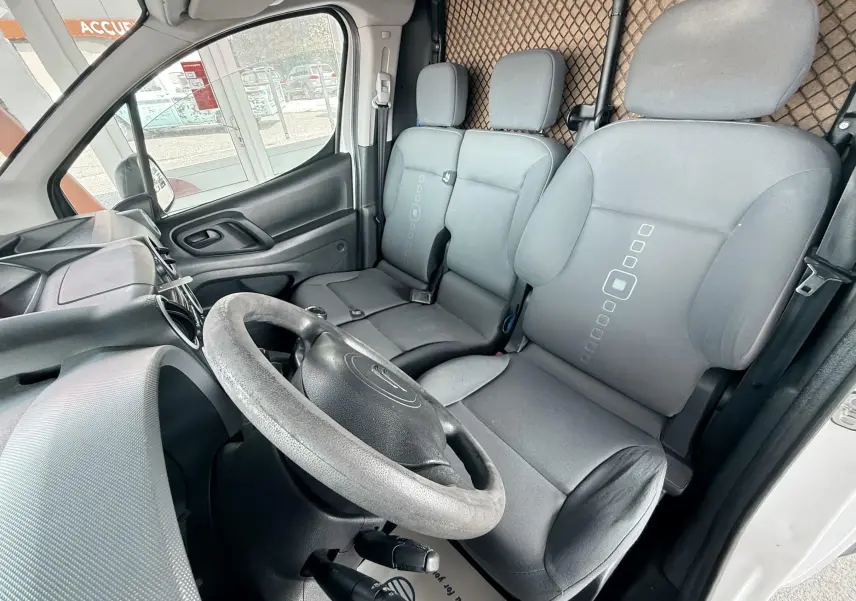 Vue intérieure côté conducteur du Citroën Berlingo blanc, sièges gris en tissu avec motifs géométriques au centre.