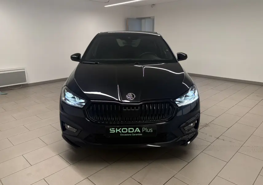 Vue avant d'une Skoda Fabia 2025 noire Magic nacré avec calandre noire et phares allumés en intérieur showroom.