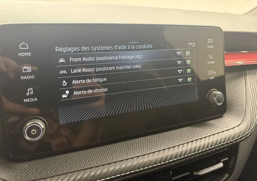 Écran tactile du tableau de bord de la Skoda Fabia 2025 affichant les réglages d’aides à la conduite, avec finition intérieure noire et rouge.