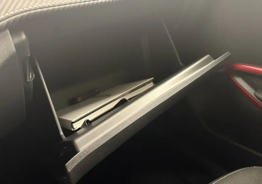 Gros plan sur la boîte à gants ouverte côté passager de la Skoda Fabia 2025 avec intérieur noir et surpiqûres blanches.