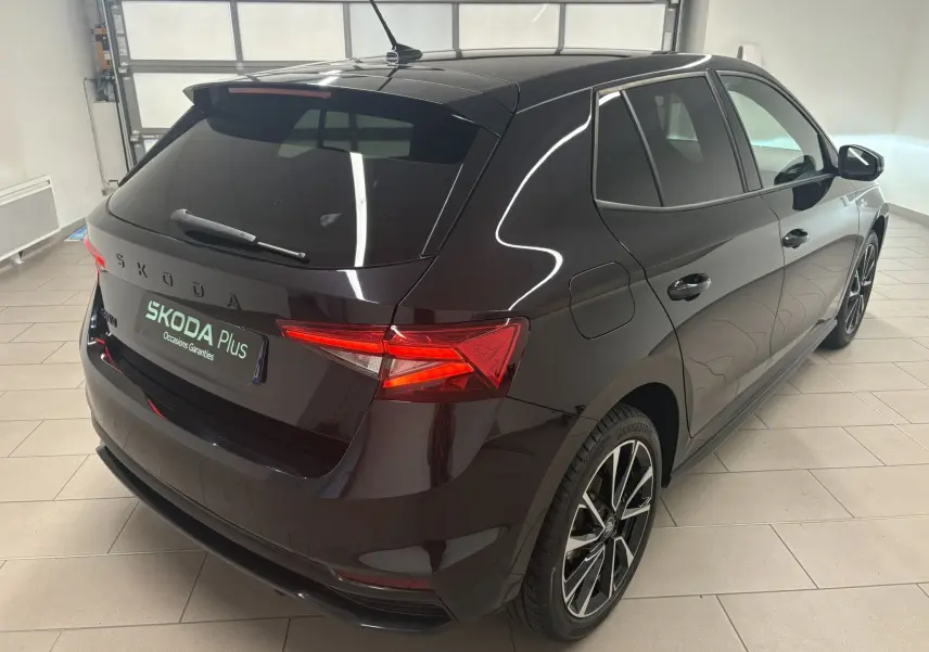 Vue 3/4 arrière droite d'une Skoda Fabia 2025 noire nacrée avec jantes alliage et feux arrière allumés en intérieur.