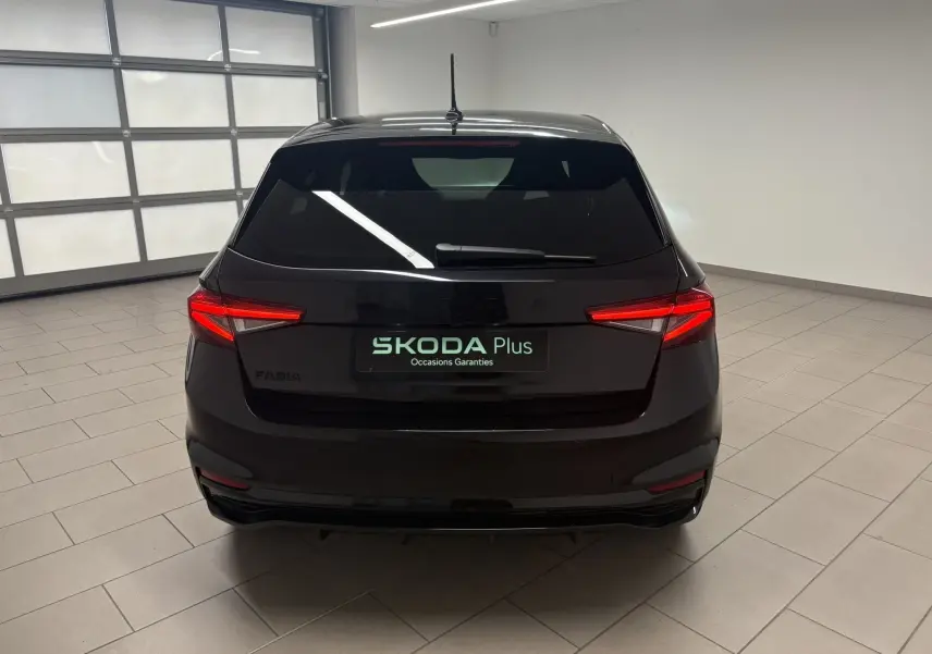 Vue arrière d'une Skoda Fabia 2025 noire nacrée, avec feux arrière allumés dans un garage lumineux.