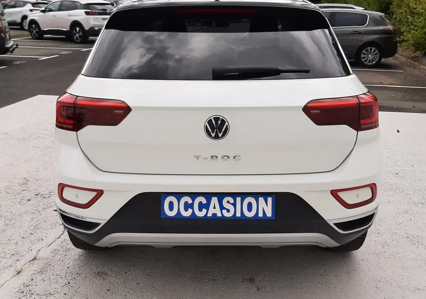 Vue arrière d'un Volkswagen T-Roc blanc pur avec toit noir, immatriculé "OCCASION", dans un parking extérieur.