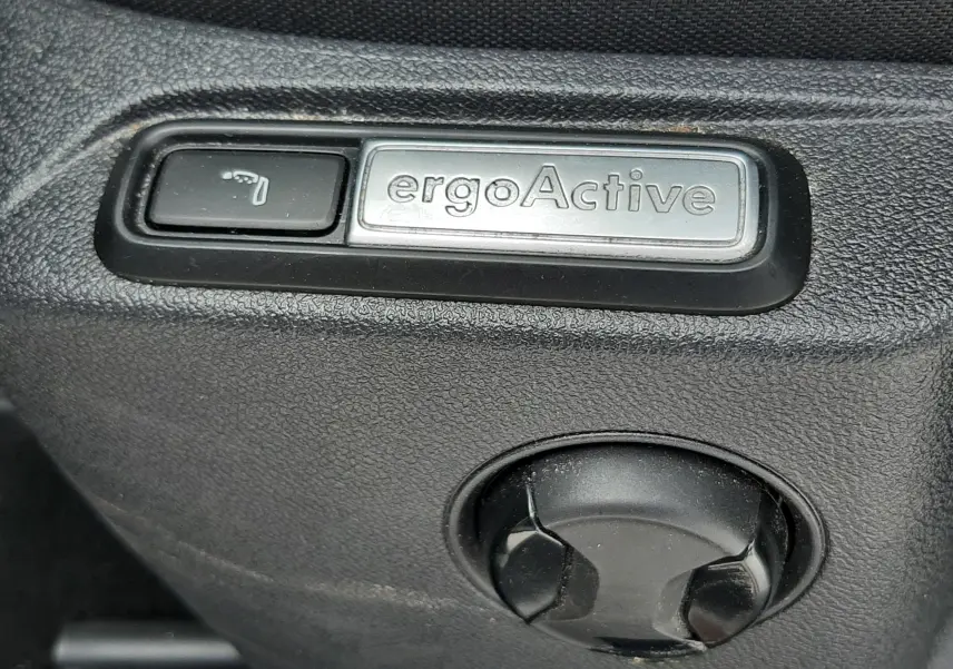 Détail du bouton ergoActive sur le côté du siège en tissu noir du Volkswagen T-Roc blanc toit noir.