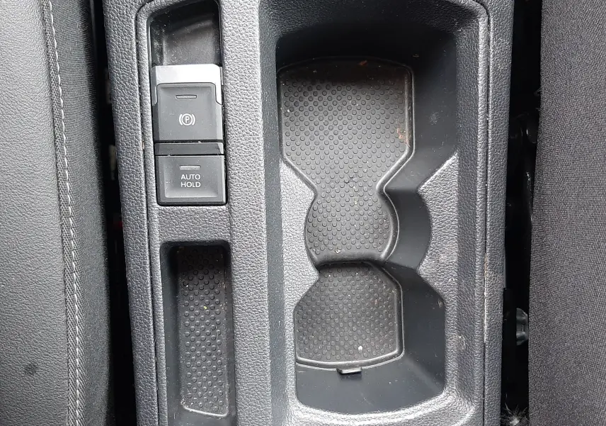 Vue plongeante sur la console centrale noire du Volkswagen T-Roc 2.0 TDI 150CH Style avec porte-gobelets et boutons de frein à main électronique.