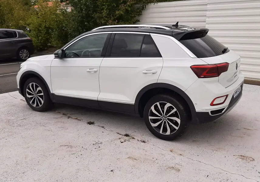 Volkswagen T-Roc blanc pur avec toit noir vu de profil côté gauche, stationné sur sol clair.